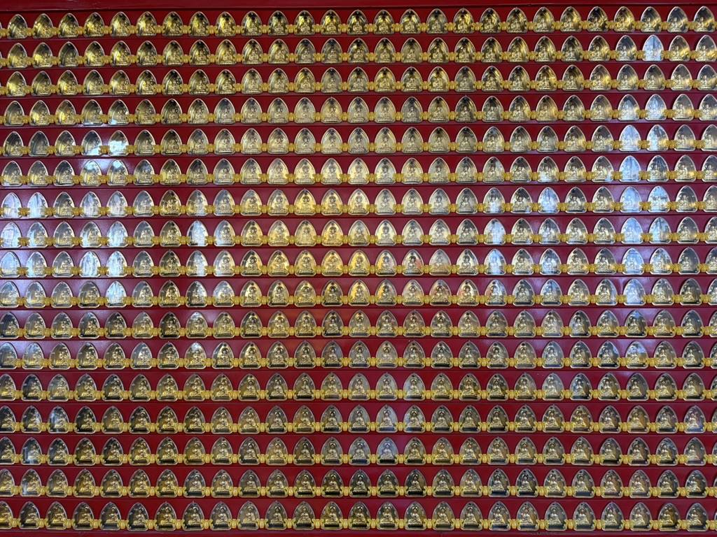 A wall of hundreds of small gilded Buddha images
